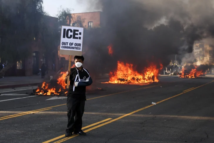  Un activista sostiene un cartel mientras los se observa a automóviles incendiados durante las protestas provocadas por las redadas de inmigración en Los Ángeles, California, EE.UU., 08 de junio de 2025. EFE/ALLISON DINNER